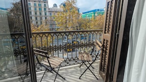 A balcony with a metal railing, a wooden bench, and a view of city buildings and trees. - Hostalin Barcelona Pg de Gràcia (Barcelona)