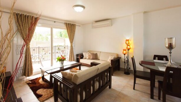 A living room with a sofa, coffee table, and dining table. There is a balcony with curtains, a lamp, and a window. - Praslin Holiday Home (Praslin Island)