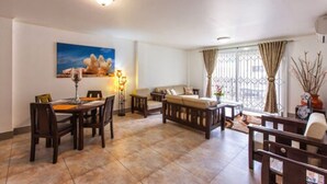 A spacious living room with a dining area, a sofa, and a large window with curtains. - Praslin Holiday Home (Praslin Island)