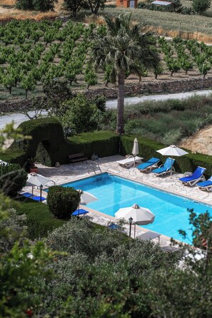 Ein Poolbereich mit Liegestühlen und Sonnenschirmen, umgeben von einem angelegten Garten und einem Weinberg im Hintergrund.