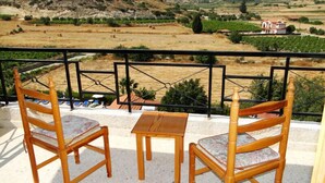 A balcony with two wooden chairs and a small table, overlooking a rural landscape with fields and a distant mountain. - Ampelokipi Holiday Apartments (Pissouri)