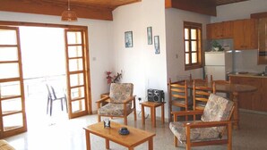 A spacious living area with wooden furniture, a dining table, and a kitchen area with wooden cabinets and a refrigerator. - Ampelokipi Holiday Apartments (Pissouri)