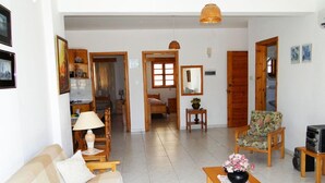 A spacious living area with a sofa, a coffee table with flowers, a chair, and a television. - Ampelokipi Holiday Apartments (Pissouri)