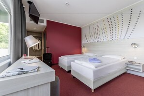 A hotel room with a bed, two bedside tables, a desk with a lamp, a suitcase, and a wall with a polka dot pattern. - Serways Hotel Remscheid (Remscheid)