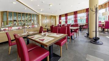 Ein modernes Restaurant mit roten Stühlen, Holztischen und einer Bar mit Glaskühlschränken.