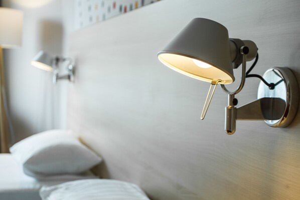 A modern hotel room with a headboard, a wall-mounted lamp, and a bed with white bedding.