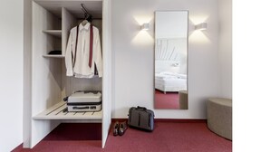 Habitación de hotel con vestidor, cama con cabecera blanca y un espejo grande.