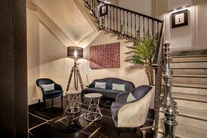 A modern lobby with a staircase, a sofa set, a floor lamp, and a potted plant.