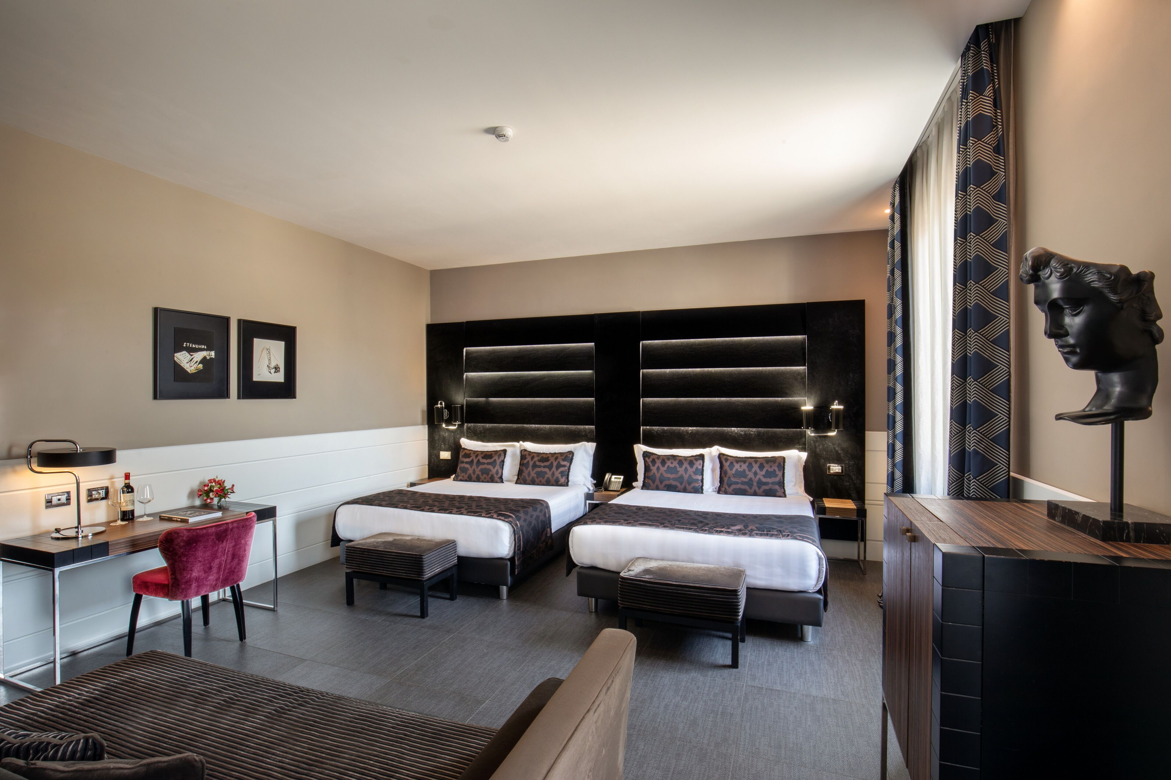 Una habitación de hotel moderna con dos camas, un escritorio, una silla roja y una estatua.