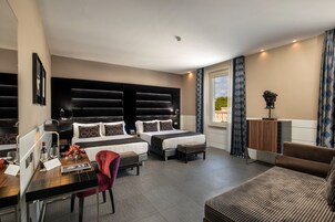 A modern hotel room with two beds, a desk, a chair, and a sofa.