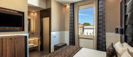 A hotel room with a bed, a TV mounted on the wall, a window with curtains, and a view of the city.