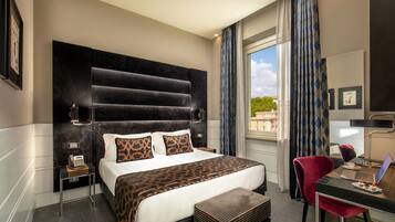 Quarto de hotel com uma cama grande, uma escrivaninha com um laptop, uma cadeira, um telefone e uma janela com cortinas.