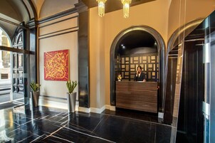 A lobby with a reception desk, two potted plants, a large abstract painting, and a chandelier.
