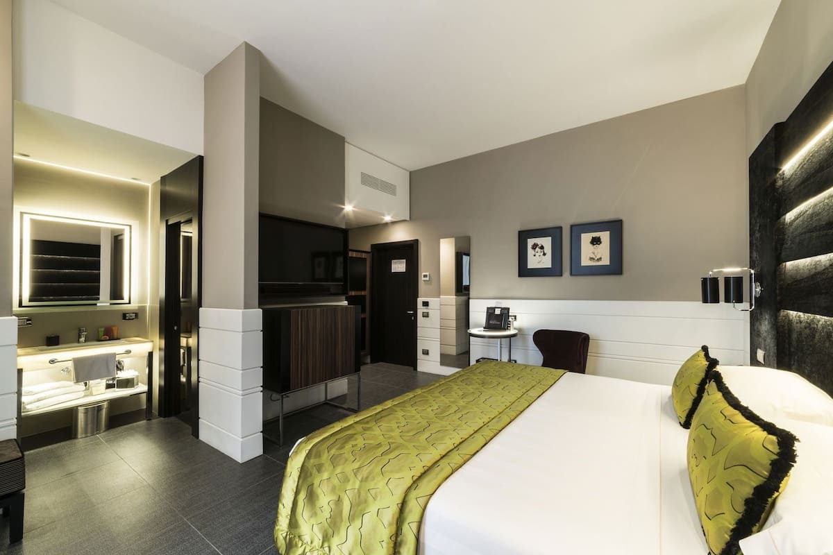Une chambre d’hôtel avec un lit, une salle de bain, un petit bureau et un téléviseur fixé au mur.