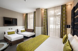 A hotel room with two single beds, a large bed, a flat-screen TV, a desk, and a chair.