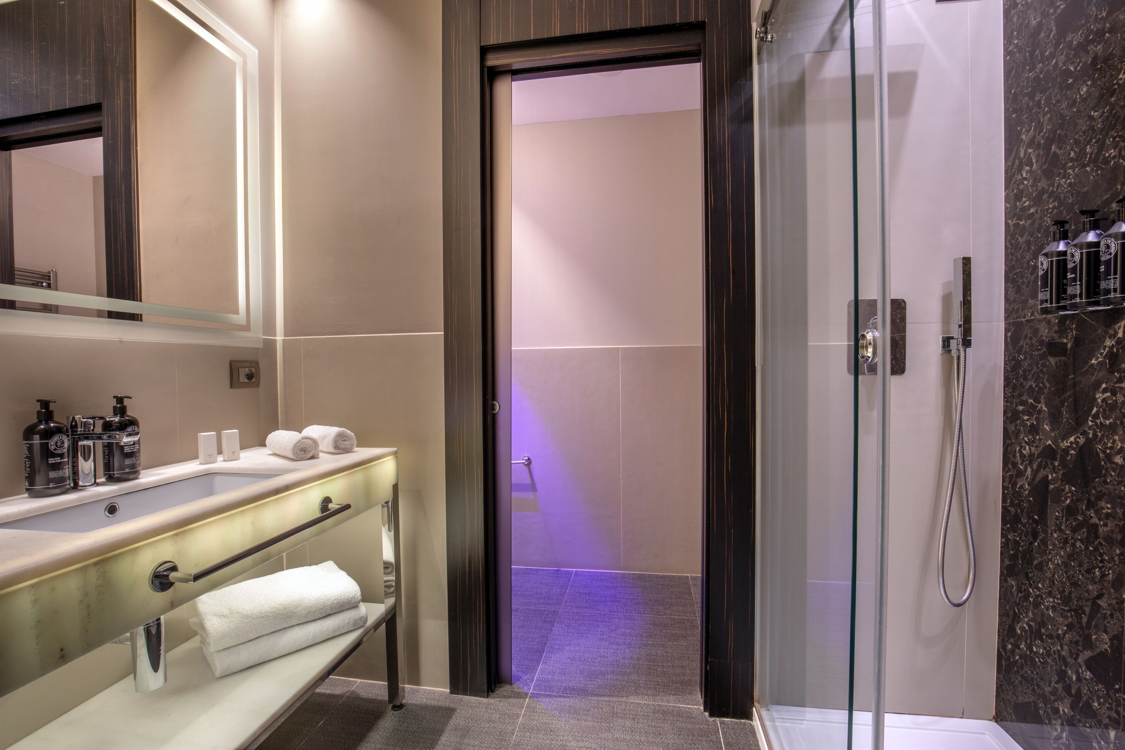 A modern bathroom with a glass shower enclosure, a vanity with a mirror, and toiletries.