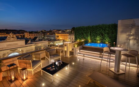 A rooftop terrace with a hot tub, seating area, and a view of the cityscape at dusk.