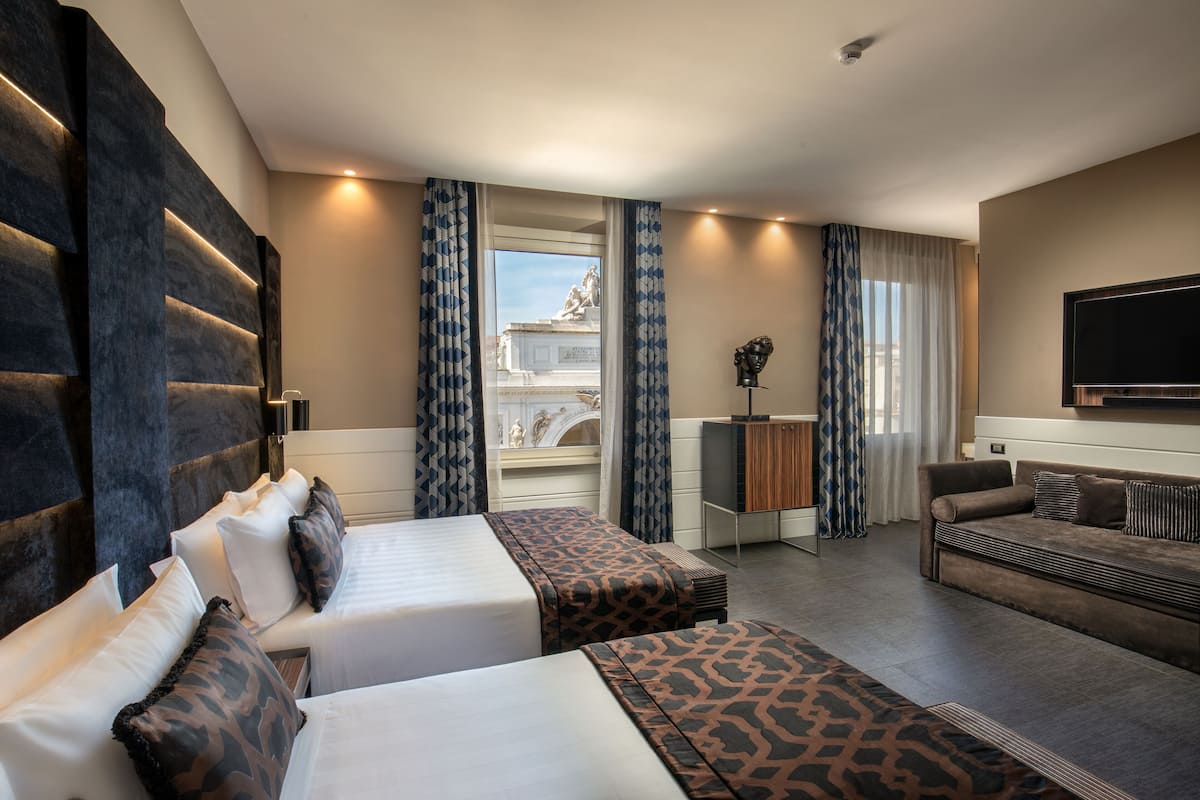 Une chambre d’hôtel avec deux lits, un canapé, une télévision et une vue sur une statue par la fenêtre.