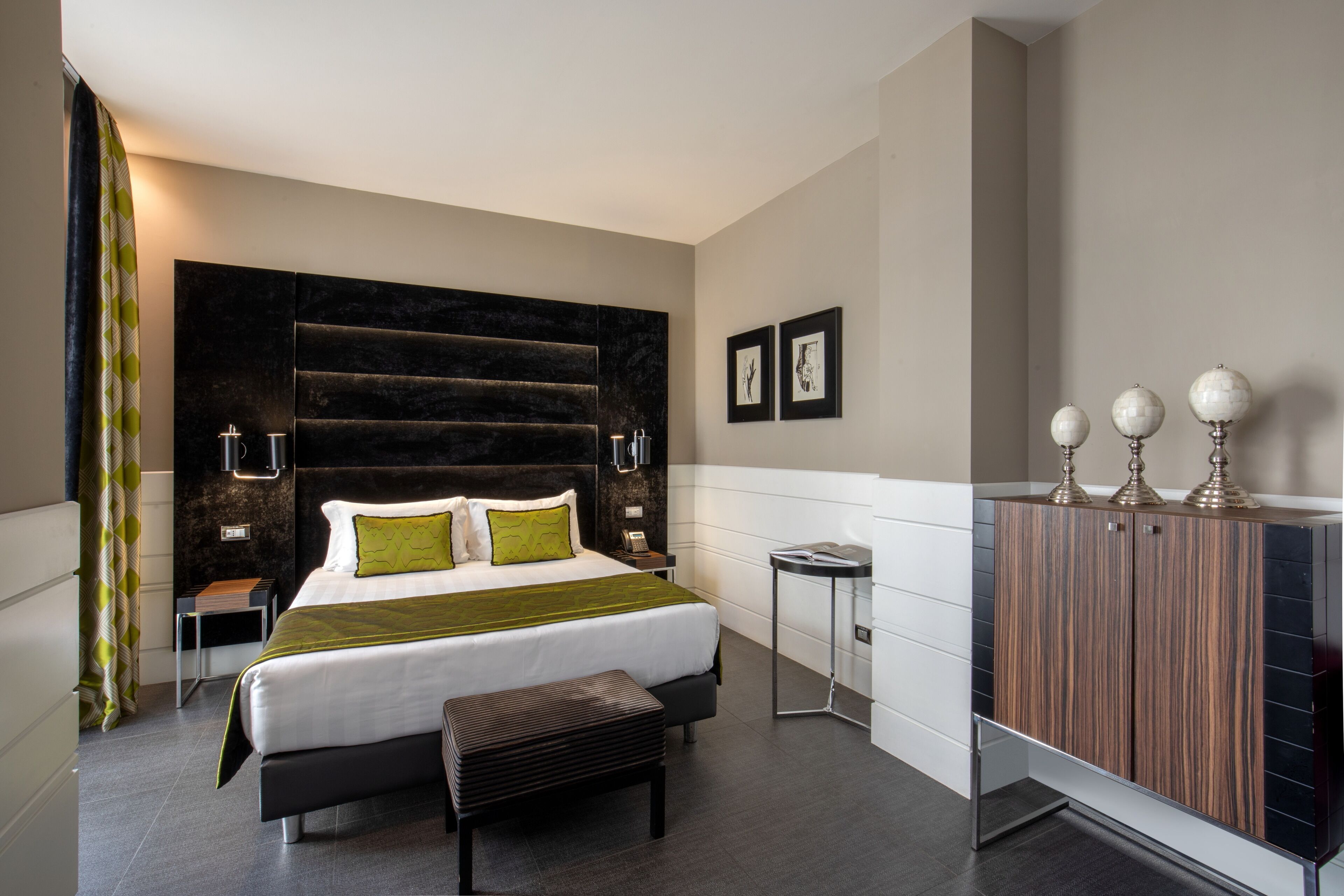 A modern hotel room with a large bed, bedside tables, a bench, a wardrobe, and a small side table.