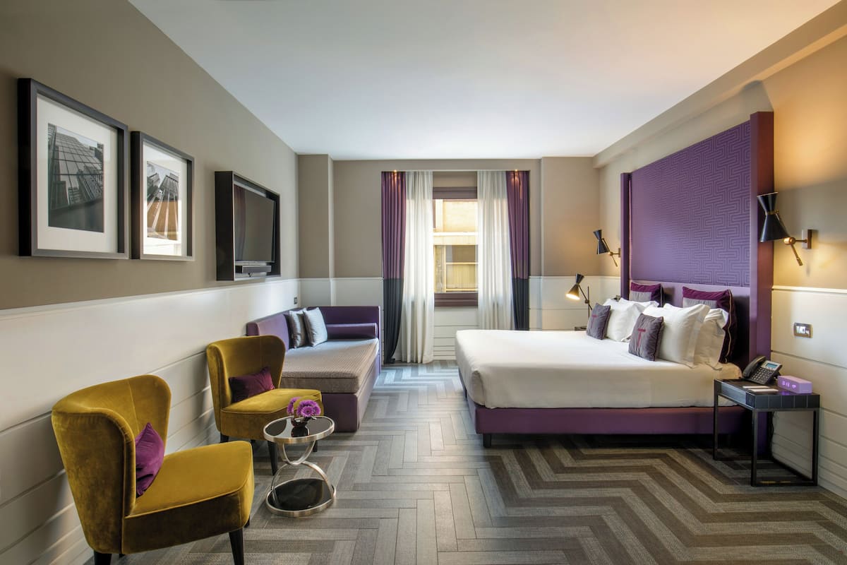 Une chambre d’hôtel comprenant un lit, deux fauteuils, un canapé, une petite table et un téléviseur.