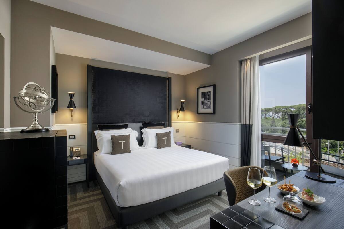 Une chambre d’hôtel avec un grand lit, une table à manger avec de la nourriture et des boissons, une télévision et un balcon avec vue.