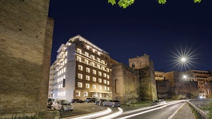 A multi-story hotel with a parking lot in front, surrounded by historic stone walls. - The Tribune, part of JdV by Hyatt (Rome)
