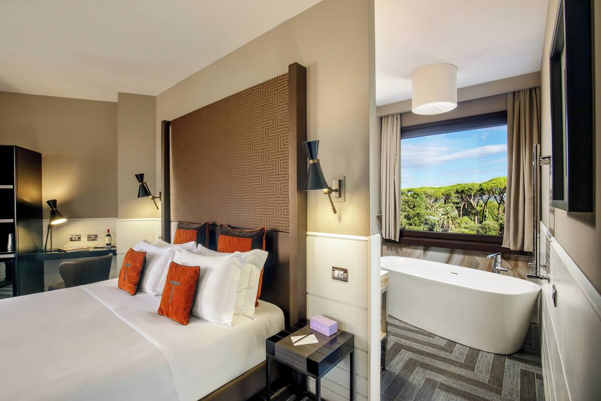 Une chambre d’hôtel avec un grand lit, un bureau, une salle de bain moderne et une vue sur la verdure.