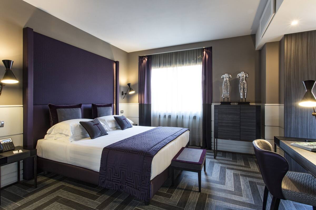 Une chambre d’hôtel avec un grand lit, des tables de chevet, un bureau avec une chaise et une fenêtre avec des rideaux.