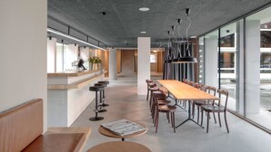 Un interior moderno con una larga mesa de madera y sillas, una zona de bar y grandes ventanales que ofrecen vistas al exterior.