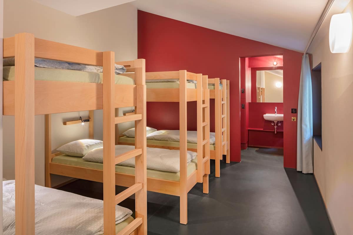 A row of bunk beds in a room with a red wall and a bathroom visible through an open door.