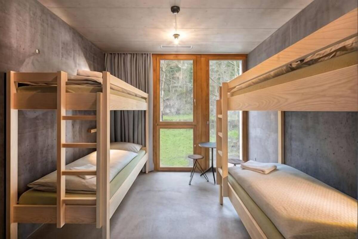 A bunk bed room with a small table and a window.