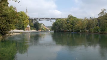 Um rio com uma ponte, árvores e edifícios ao fundo.