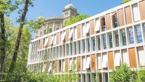 Un edificio moderno con grandes ventanales y un edificio clásico al fondo.