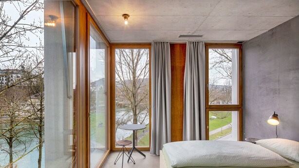 Un dormitorio moderno con ventanas amplias, una mesita pequeña y una lámpara.