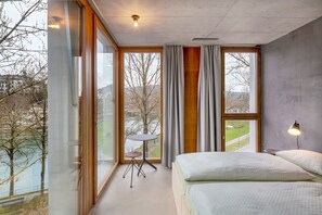 A modern bedroom with large windows, a small table, and a lamp. - Youth Hostel Bern (Bern)