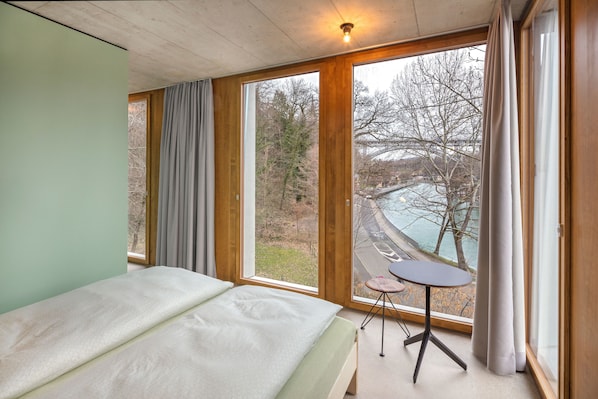 A bedroom with a bed, a small table, and a view of a winding road and trees. - Youth Hostel Bern (Bern)