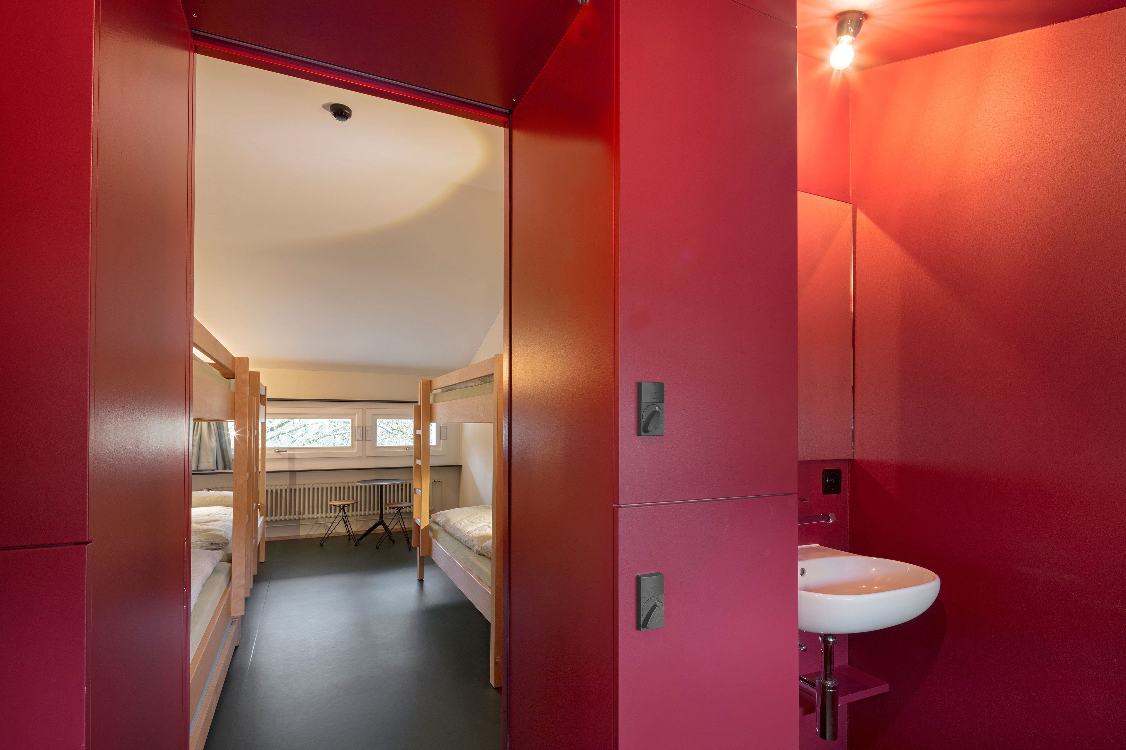 Ein Zimmer mit Etagenbetten, einem Heizkörper, einem Fenster und einem Waschbecken.