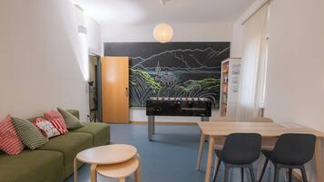 A room with a green sofa, a wooden table, and a foosball table.