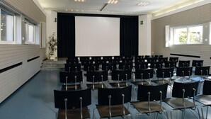 A conference room with rows of chairs, a large screen, and windows. - Youth Hostel Locarno (Locarno)