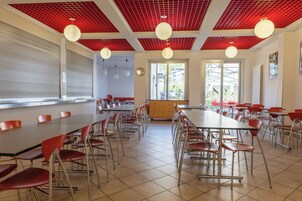 Un comedor amplio con sillas y mesas rojas, techo rojo y ventanas grandes que permiten la entrada de luz natural.