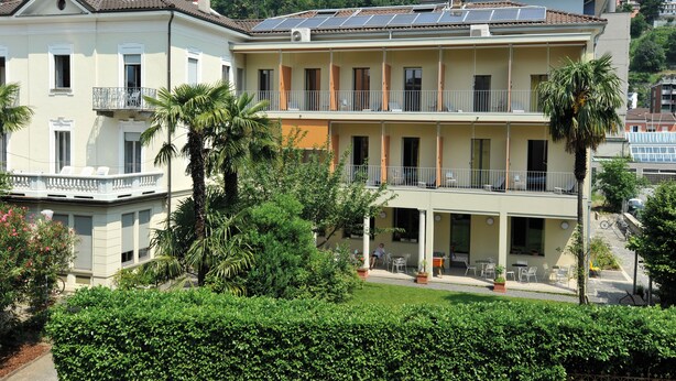 A two-story building with balconies, solar panels, and a garden area with outdoor seating. - Youth Hostel Locarno (Locarno)