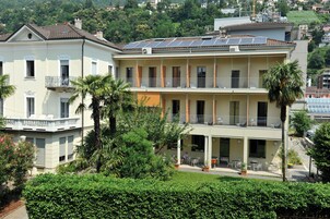 Un edificio de dos pisos con balcones, paneles solares y un jardín con mobiliario exterior.
