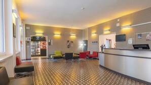 A reception area with a patterned floor, seating arrangements, a refrigerator, and a television mounted on the wall. - Youth Hostel Locarno (Locarno)