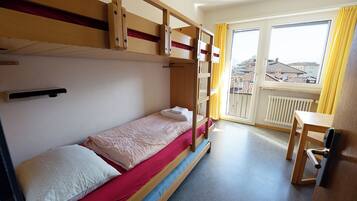 A room with bunk beds, a desk, and a window with yellow curtains.