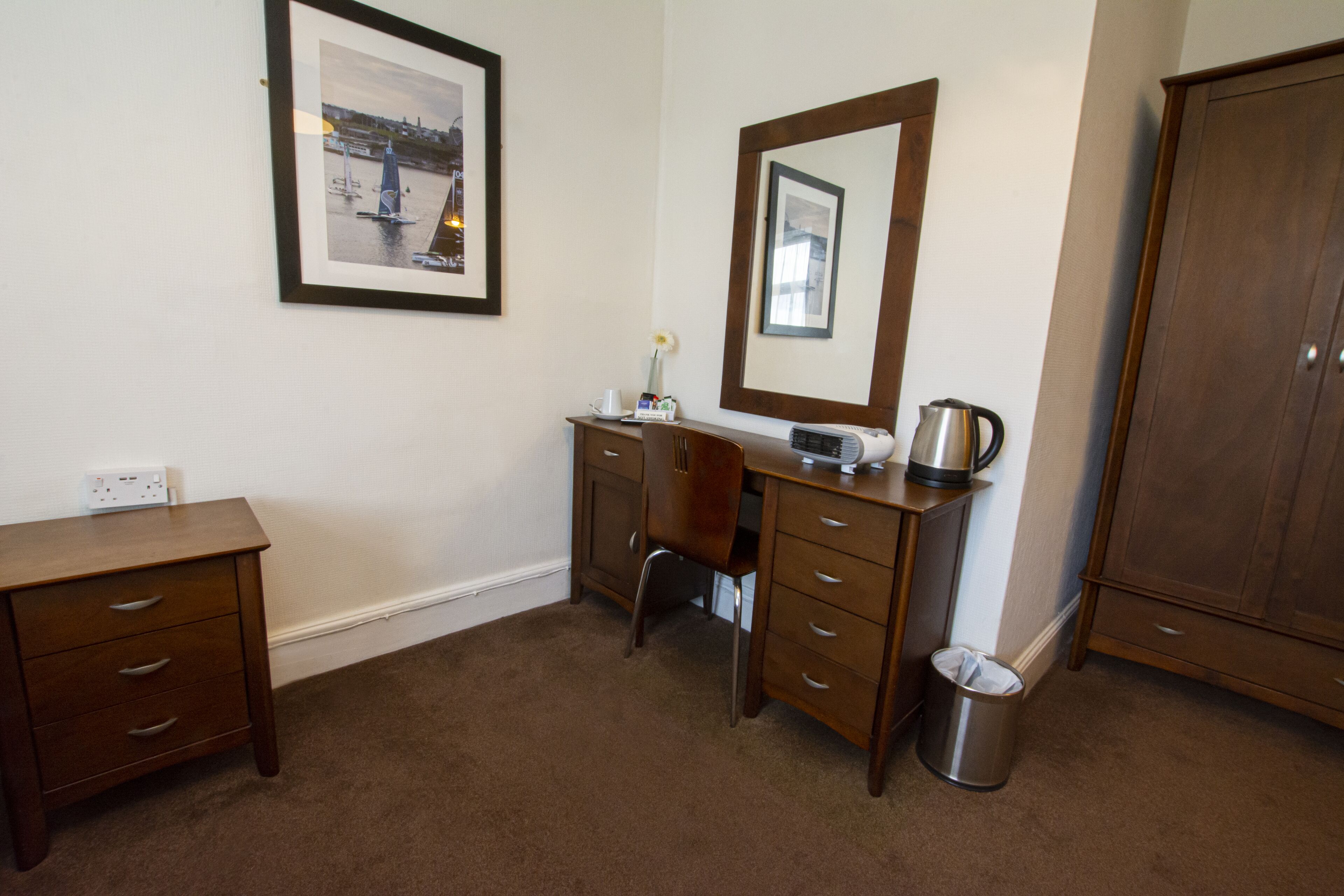 A bedroom with a wooden dresser, a chair, a desk, a mirror, and a wardrobe.