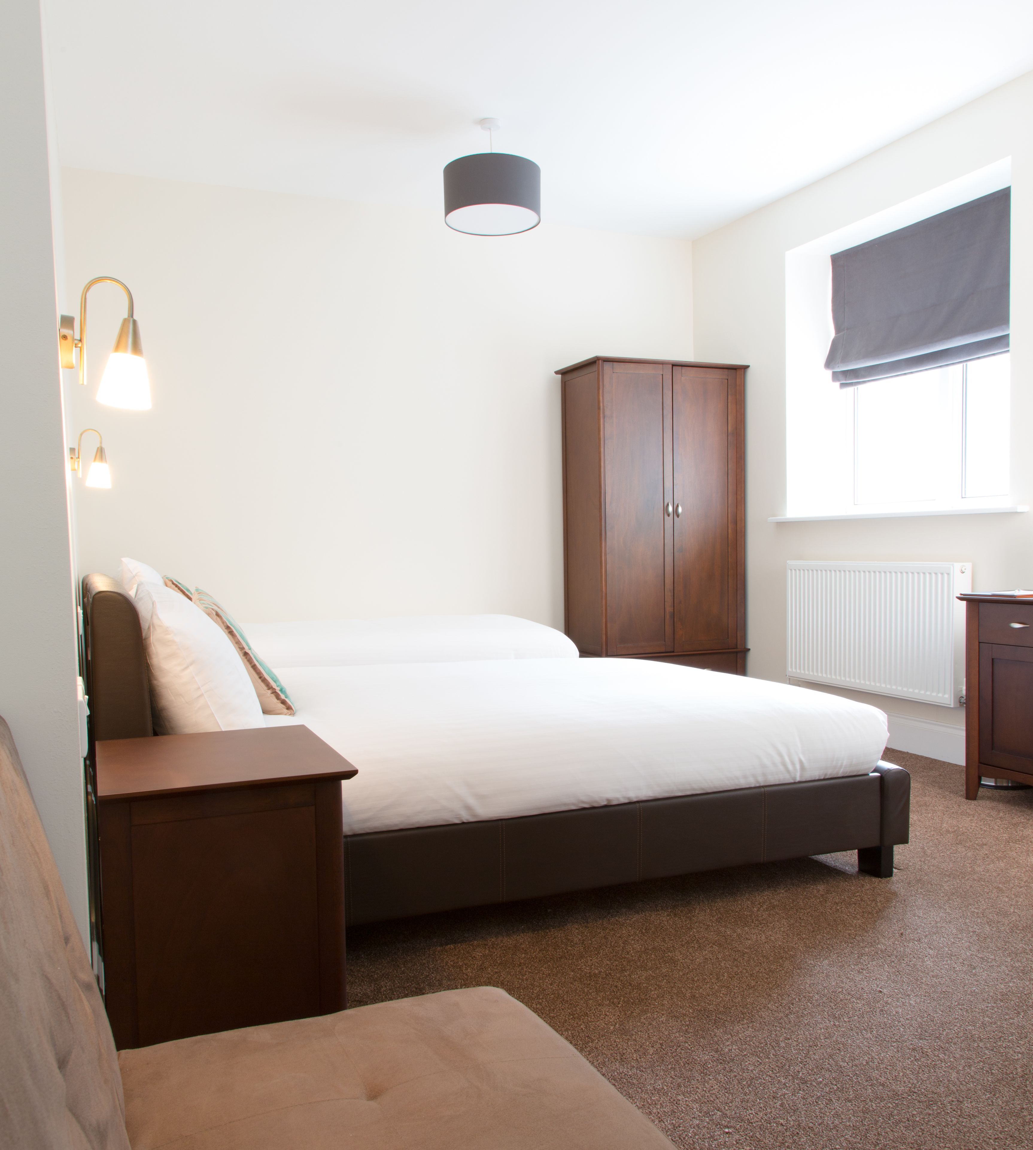A bedroom with a bed, a wardrobe, a nightstand, and a window with blinds.
