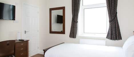 Un dormitorio con cama, cómoda, televisor montado en la pared, ventana con cortinas y espejo.
