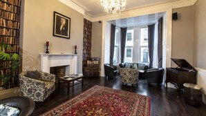 Een ruime woonkamer met een open haard, een groot tapijt en een piano.