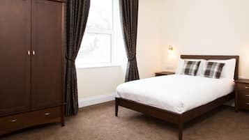 Une chambre à coucher avec un lit en bois, une table de chevet, une armoire et une fenêtre avec des rideaux.