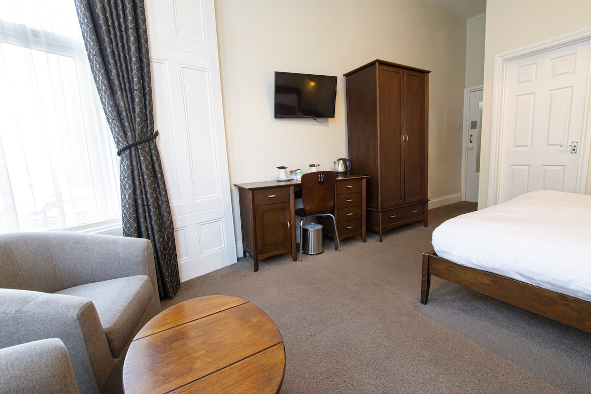 A hotel room with a bed, a desk with a chair, a television, and a wardrobe.